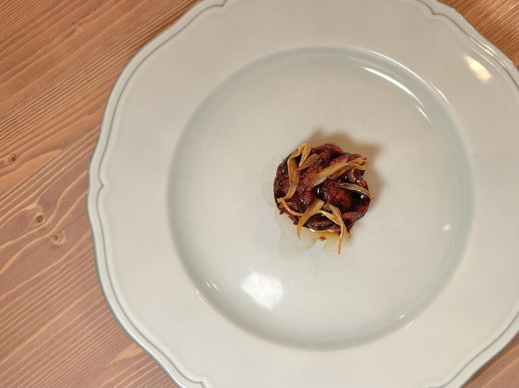 Pomodoro, pane e scalogno. Interpretazione di un pasto contadino, pane, pomodoro e cipolla. Alla base c’è un battuto di pomodoro gratinato, ottenuto cuocendo i pomodori in forno per circa quattro ore così da concentrarne l’aromaticità. Sopra, una panzanella condita con acqua di pomodoro, olio extravergine d’oliva e aceto di vino rosso invecchiato. Completa il piatto un pomodoro lentamente essiccato in forno, poi passato alla brace, laccato con un fondo di cipolla e rifinito con scalogno prima disidratato e poi reidratato nella salsa ponzu. Piatto di muscoli veg, di intensità aromatica