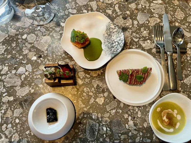 Le entrée del menu a mano libera "A modo mio": in alto, Carota in brunoise e crema, mandorle tostate e in crema e salsa al prezzemolo; appena sotto a destra Dosa di lenticchie e riso con ripieno di mutabal e prugne; in basso a destra Zuppetta fredda di zucchine trombetta, con uova di salmerino affumicate, kefir di capra e spolverata di cannella, in basso a sinistra Frutta nera, un cubo di mela annurca macerata a lungo, appena sopra un Handroll con alga nori, riso cinese al vapore e tartare di trota trentina marinata al garum. Chiude tutto un assaggio di erba ghiaccio, a pulire e preparare per gli assaggi successivi