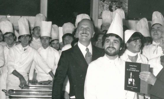 Una foto dei primi anni Ottanta: in primo piano Gianluigi Morini e un giovane e barbuto Valentino Marcattiliii. Si nota qualcuno che tiene in mano il libro A tavola al San Domenico, uscito nel 1982, l'autore è proprio Morini con le ricette di Marcattilii. Un pezzo di storia gastronomica
