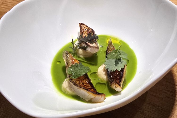 Triglia leggermente scottata, mousse di ceci e insalata liquida di lattuga, sale e olio. Primo dei tre amuse bouche, apre con raffinato equilibrio tra texture e contrasti gustativi misurati. La cremosità vegetale della mousse dialoga con l’umami del pesce, mentre l’insalata liquida conferisce freschezza e leggerezza. Segue la crème caramel con topinambur, caramello di melassa di carruba e fondo vegetale, un’idea interamente vegetale di grande intensità e suggestione
