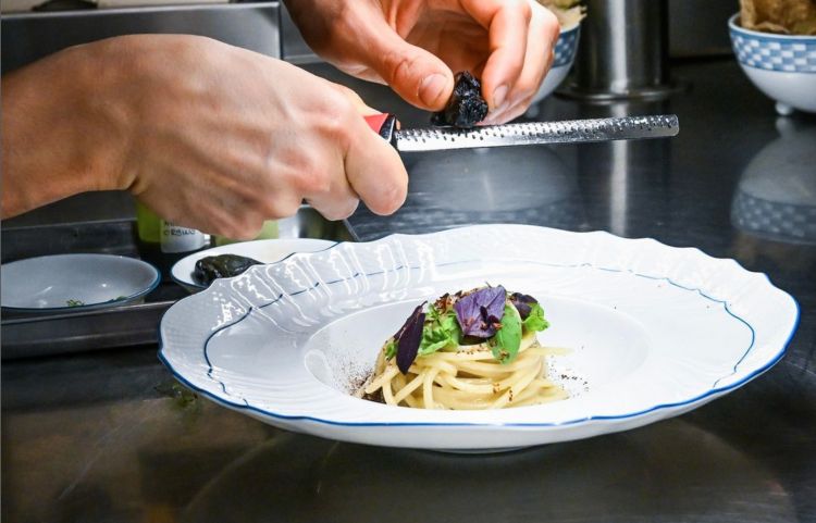 Spaghetto alle vongole affumicate, mantecato alla crema di vongole, precedentemente affumicate con aggiunta di limone salato, cinque varietà di basilico (thai, greco, genovese, viola e limonato) e un olio al prezzemolo. Un classico smontato e rimontato, senza la vongola nel piatto, con acqua di vongole disidratata e grattugiata a conclusione del piatto, come fosse una bottarga
