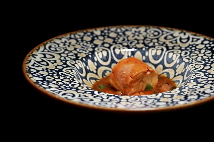 Spigola, sauce vierge e suggestioni di sardenaira: la parte della pancia della spigola viene lavorata con una riduzione di pomodoro all’interno di una preparazione ispirata a una blanquette francese, quindi arrotolata e cotta esclusivamente al vapore. Alla base c’è una sauce vierge (pomodoro, capperi, limone ed erbe di Provenza). Il piatto si chiude con elementi che richiamano la sardenaira ligure: pomodoro, origano, colatura di acciughe, peperoncino in infusione e olio all’erba cipollina. Al palato, la spigola regge tutto sommato l'urto deciso dei condimenti, che han tanta personalità, sapidità e anche una piacevole piccantezza: piatto goloso, pieno