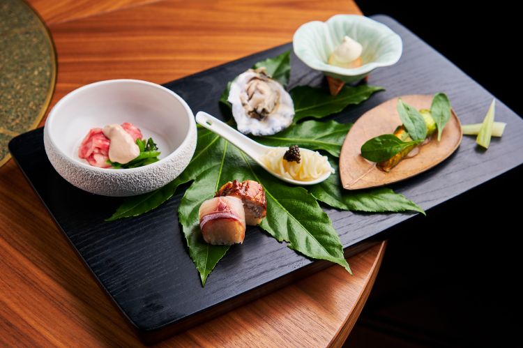 Hassun
Hassun è il cuore di ogni percorso kaiseki, un'insieme di piccoli assaggi (8, nel nostro caso) di terra e di mare, una preziosa istantanea della stagione in cui stiamo.
Si parte dal cucchiaino al centro: dei Somen sbollentati in brodo di vongole, con caviale. Da sinistra in alto, in senso orario: Wagyu shabu shabu con salsa kurumi (ponzu e noce); Ostrica cotta al vapore con succo di limone; Shiraae, un piccolo contorno veg, in questo caso insalatina di tofu e pesche bianche; due piccoli tocchi di Sedano agrodolce in salsa agro-dolce amazu; Fiori di zucchina ripieni con capesante e spinacino e, in basso a sinistra, due esempi di bozushi (sorta di roll al contrario), in questo caso di anguilla affumicata e branzino