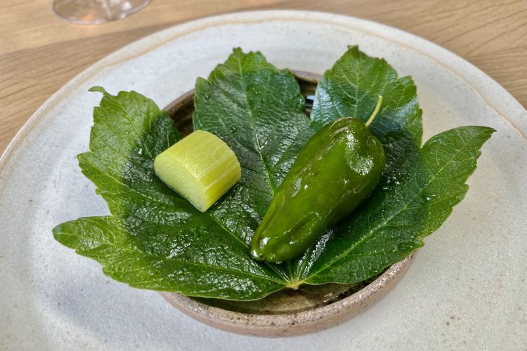 Grilled padròn pepper
La parte commesitibile è a destra: è un peperone verde cotto al barbecue, svuotato, riempito con insalata di baby cetrioli e fragole verdi, semi di girasole aromatizzati con una pasta di olio e chile morita leggermente piccante. A sinistra una fettina di rabarbaro verde molto acquosa, lavorata in brine, una salamoia di acqua e sale, normalmente utilizzata per la marinatura delle carni. Non si mangia ma si spreme sul peperone verde prima dell'assaggio, come fosse una fettina di limone
