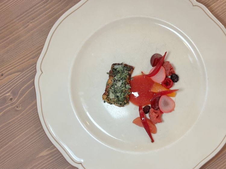 Anguilla alla brace, macedonia di frutta e verdura. L’anguilla viene laccata alla brace con una salsa teriyaki a base di anguilla, miele, zenzero e alghe. Dopo un passaggio a vapore, viene servita con nepeta essiccata e zest di limone. A fianco, una macedonia di frutta e verdura: cipolla, ravanello e rapa rossa marinati sotto aceto; susine e pesche fermentate; anguria congelata e scongelata più volte, così da romperne le fibre, eliminare parte dell’acqua e renderne il morso più consistente; more ghiacciate. A completare, una salsa di susine. Piatto quasi tranquillo, ben gestito