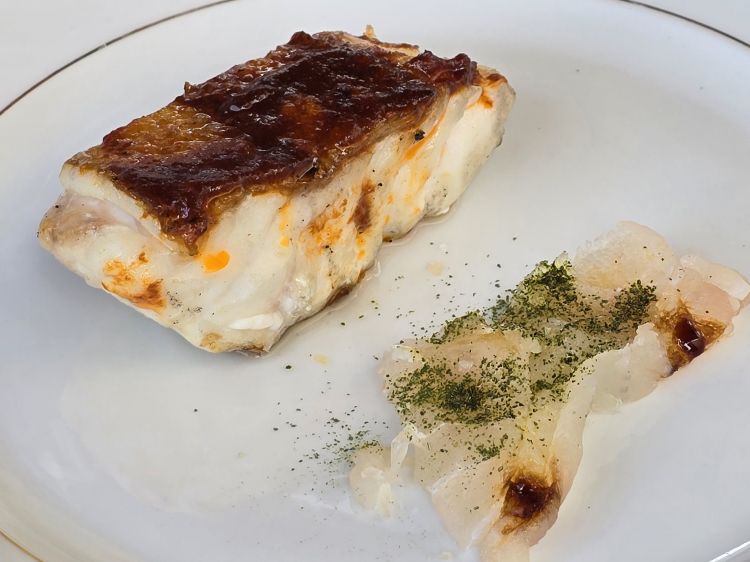 Cernia frollata cruda e cotta. È un piatto che celebra la versatilità della cernia e l’arte della cucina sostenibile. Il pesce viene da un processo di frollatura durato 8/10 giorni e viene servito con una salsa di aglio, cipolla, teste di gambero, zenzero, olio, peperoncino. La parte cotta passa dal forno Josper e si caratterizza per la croccantezza della pelle. Anche qui sapori netti, sapidità, dolcezze levigate e affumicature e l’intrigante battaglia di consistenze dove il crunch della pelle diventa primo attore