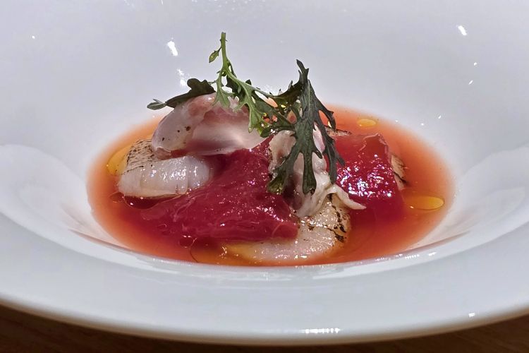 Capasanta con anguria alla brace, dressing di anguria, basilico e guanciale di suino Nero dei Nebrodi. Un piatto che seduce con un gioco intrigante di dolcezze umami e grassezze, bilanciate da contrappunti acidi che ne affinano profondità gustativa e persistenza
