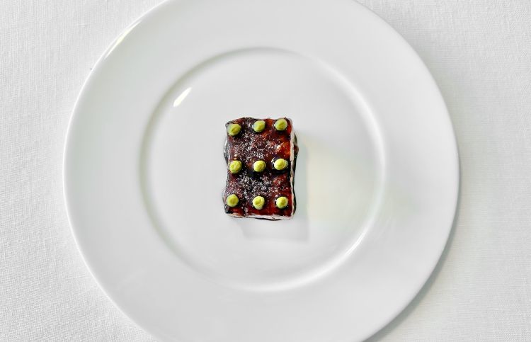 Melanzana arrosto e rosmarino - È uno dei piatti iconici. La melanzana viola viene utilizzata per il cubo alla base, che dà struttura, mentre la melanzana nera diventa un caramello che forma la glassa superiore. Le piccole punte verdi sono estratto di rosmarino, che introduce una nota profumata e balsamica. La versione precedente prevedeva invece caramello di pesca e concentrato di pomodoro; quella servita qui viene presentata come la versione attuale del piatto storico. Iconico