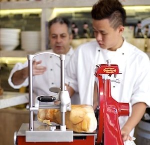 Alle spalle, Mario Caramella osserva attenato un collega di Singapore alle prese con un'affettatrice