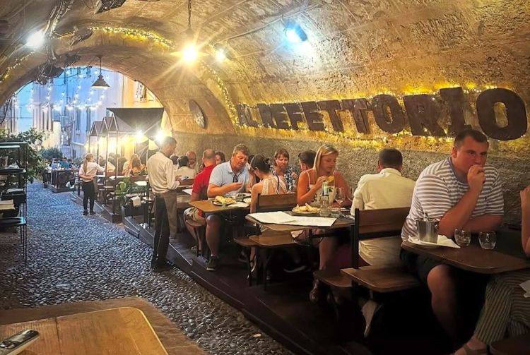 Tavoli all'aperto Al Refettorio. Il ristorante si trova nel centro storico di Alghero, in Vicolo Adami 47, a pochi minuti da Piazza Civica e dai bastioni. Il locale si sviluppa in parte sotto i portici di Vicolo Adami, con tavolini all’aperto ma coperti dalle arcate, mentre all’interno c’è una sala ristorante più raccolta