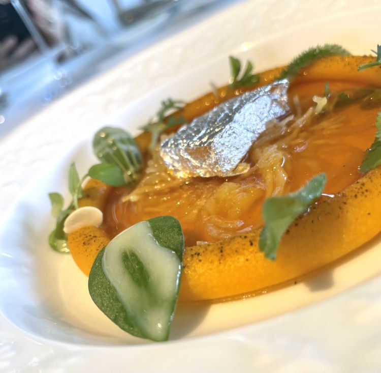 Zucca e spezie
Si parte da una zucca giapponese detta zucca spaghetti per la particolarità della sua polpa a filamenti che ricordano tanto i capelli d'angelo, solitamente usati per brodini e pastine. Ed è proprio con questi filamenti che Quadrio giunge all'idea di una pastina 100% vegetale: la zucca viene passata in forno e una volta cotta se ne estraggono i filamenti dorati serviti con purea di zucca Delica, semi ed erbe e un brodo, in realtà kombucha calda di zucca alle spezie. Infine, come ogni pastina che si rispetti, si aggiunge un formaggino, anche in questo caso 100% vegetale a base di mandorla