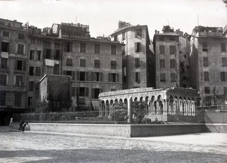 Bedin non è solo una trattoria, ma un piccolo fossile gastronomico della Genova scomparsa. La sua storia sta tutta nel passaggio da piazza Ponticello alla moderna Piazza Dante, qui in una foto di molti decenni fa. La tradizione fa risalire la nascita di questo locale almeno al 1862, o comunque ai primissimi anni dopo l’Unità d’Italia: fu tra le prime licenze concesse a Genova dopo l’Unità, ma il locale esisteva già prima come “farinotto” di quartiere, specializzato in farinate e torte salate. Il cuore originario era Piazza Ponticello, zona vivissima appena fuori Porta Soprana, poi cancellata dalle grandi trasformazioni urbanistiche tra fine Ottocento e anni Trenta. Piazza Dante, infatti, nasce quando viene demolito l’antico quartiere di Ponticello nell’ambito del “Piano delle aree centrali”; la piazza attuale è del 1937. La Bedin era lì, in quel mondo di botteghe, vicoli, fontane, mestieri. Una ricostruzione su Genova antica colloca la celebre Bedin in Via Rivotorbido, presso piazza Ponticello, e la ricorda appunto per le sue farinate; aggiunge che il negozio ebbe poi altre collocazioni. Nella collocazione più recente, la si trova in Piazza Dante, all’imbocco della Galleria Colombo, cioè proprio nell’area che ha sostituito Ponticello
