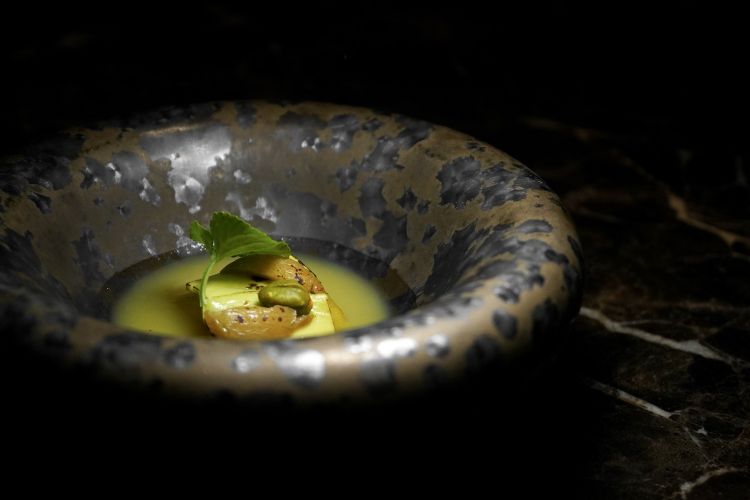 The leek: it is baked in Verjus, finished on the bbq and accompanied by slices of avocado marinated in sake. On the base, leek water flavoured with apple cider and drops of dandelion oil. On the surface: sweet and sour grapes, pistachios and violets
