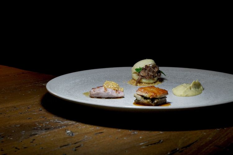 Agnello, yogurt di capra, ceci, menta, senape. Il carrè di agnello, a sinistra, viene rosolato in padella e condito con la senape; la pancia, in basso, viene cotta al vapore e a sua volta rosolata; in alto, il coscio stracotto farcisce un panino di semola, con yogurt di capra, menta e ceci soffiati alla base. A destra, infine, una crema di ceci
