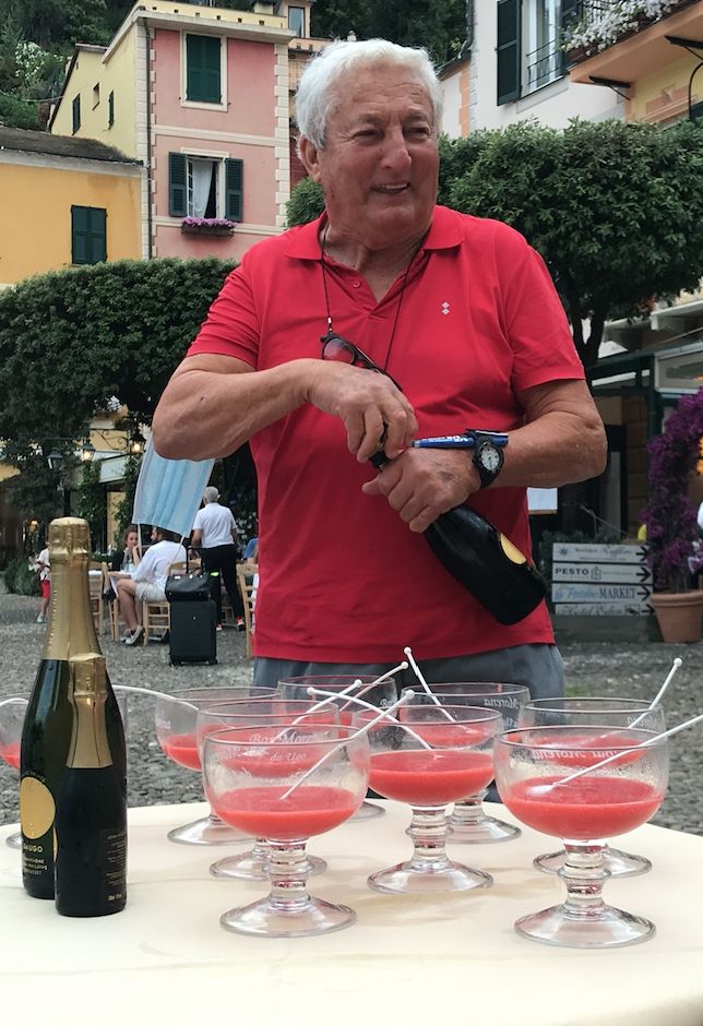 Ugo, lo strorico anfitrione del Bar Morena della Piazzetta di Portofino mentre prepara il cocktail Bellini: polpa di pesca e champagne della cuvée Da Ugo
