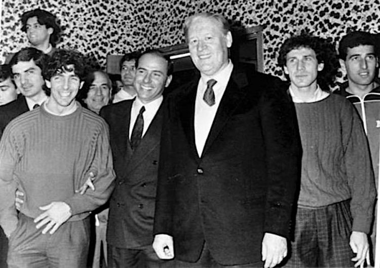 Silvio Berlusconi, da poco presidente del Milan, in visita al centro tecnico di Milanello nel marzo 1986, posa tra l'allenatore Nils Liedholm e Paolo Rossi. Sulla destra Franco Baresi e in tuta Mauro Tassotti
