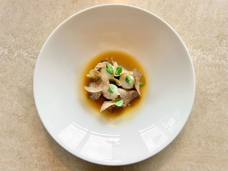 Bottoni di carciofi, salsa di pollo arrosto, capasanta e tartufo nero. I bottoni sono ripieni di fondente ai carciofi, nascosti dai carciofi, dalle capasante e dal tartufo, completati infine con ristretto di pollo