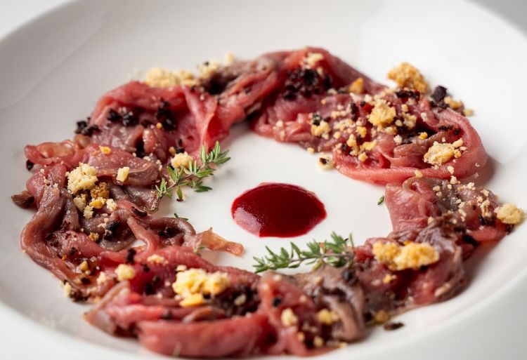 Uno dei piatti serviti al ristorante Tavern ad Arqu&agrave; Petrarca: Carpaccio di cinghialetto euganeo, marinato con timo e lime dell'orto, arricchito da un tocco croccante di crumble e dalla profondit&agrave; della polvere di olive locali
