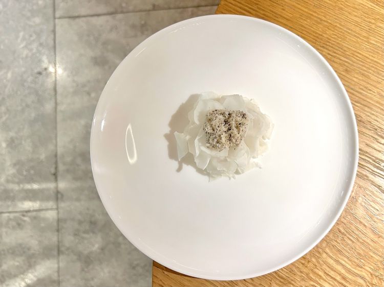 Cavolfiore, lavorato in tutte le sue forme e consistenze: crema di cavolfiore, le sue cimette ossidate e in pickles, il suo gambo crudo e tagliato a velo con tartufo bianchetto, poi erbe aromatiche e polvere di caffè brasiliano