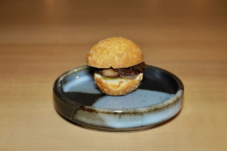 Panino con cipolla rossa caramellata e collo di maiale marinato in salsa tare, un omaggio dello chef a suo papà Mimmo, «uno storico "paninaro”». Il collo di maiale viene cotto a bassa temperatura e poi marinato in salsa di soia. sake, mirin, katsuobushi e alga kombu
