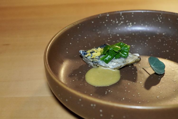 Sgombro waraiaki con emulsione di mare, zest di limone, lime e spinacino saltato. «Lo sgombro viene marinato in aceto di riso, poi cotto alla waraiaki, una cottura giapponese con il fuoco del fieno». L'emulsione è di cozze
