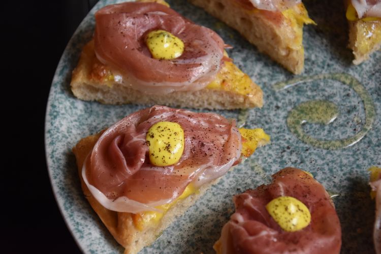 Pizza al padellino Nera Sicula. Realizzata in doppia cottura con impasto di farina di tipo 1 e Maiorca, prima viene cotta a vapore a 130 gradi, poi sottoposta a una seconda cottura statica nel forno a 250 gradi. La combinazione di ingredienti: piacentino ennese, prosciutto crudo, miele di ape nera sicula e una delicata polvere di caffè
