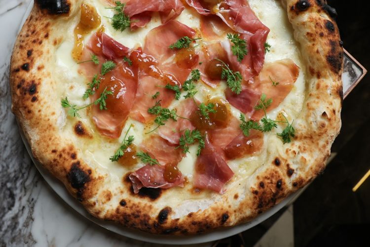 La Pizza e fichi di Fonderì: crema di fichi, provola affumicata, crudo di Parma stagionato 20 mesi, germogli di carota e olio EVO