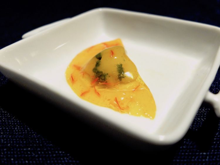 Raviolo d'acqua allo zafferano ripieno di gambero crudo e pesto. Il raviolo è fatto con un'infusione di zafferano gelificata
