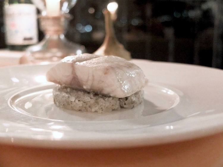 Trancio di branzino selvatico in crosta di sale, fieno, camomilla e carciofo in casseruola. È servito su una base di sale