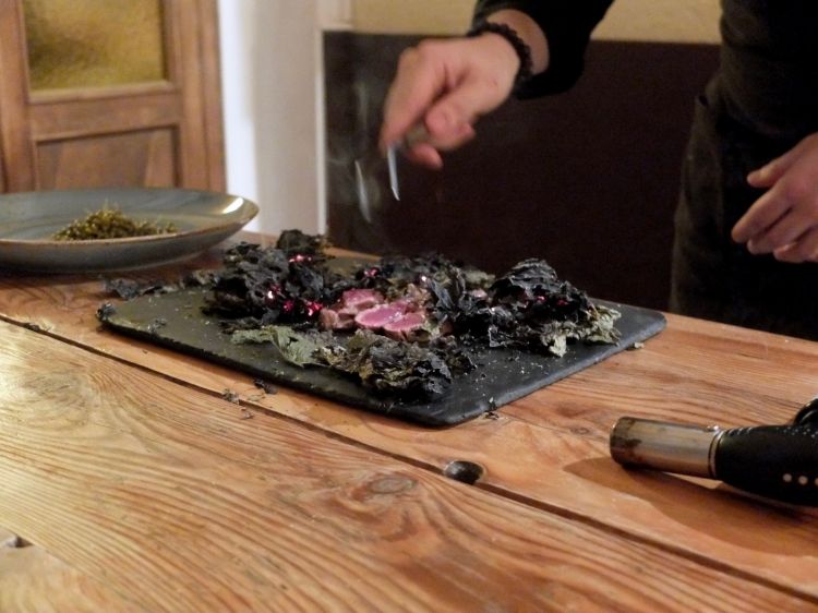 Al tavolo viene scottato un filetto di pecora gigante bergamasca racchiuso in foglie di frassino fermentate