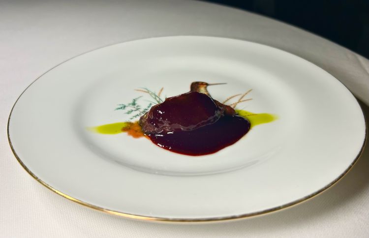 Colombaccio - Proteina. Il colombaccio viene affrontato in modo opposto rispetto alla tradizione delle cotture lunghe, che appiattiscono il gusto e rendono la texture stopposa. Qui si sceglie, per il petto, una cottura violenta esclusivamente dal lato della pelle, seguita da un periodo di riposo, senza frollatura, con l’intento di preservare e valorizzare la complessità della carne. È servito su un sugo ottenuto dallo stomaco, con salsa di amarene selvatiche e olio all’alloro. Il filetto, a parte, viene marinato nel suo stesso grasso arrostito