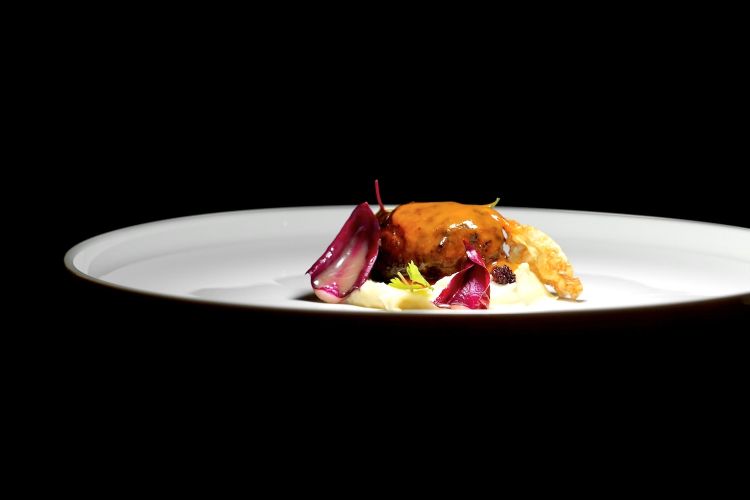 Crepinette di coda: la coda viene lavorata come fosse un pulled pork e poi avvolta dalla rete di maiale, condita col suo fondo e nappata con burro ed erbe aromatiche. Il tutto è accompagnato da purea e chips di sedano rapa e radicchio tardivo ai lamponi