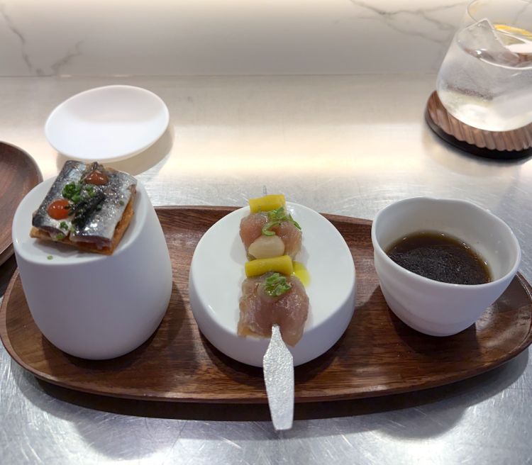 Il benvenuto dalla cucina: Brodo di pesce e olio agli agrumi, Spiedino di tonno marinato e Sardina marinata. Il nostro percorso inizia con tre stuzzichini di benvenuto che richiamano subito il mare: un trittico d’apertura che mette subito in chiaro la direzione della cucina, quindi, materia prima marina protagonista, sapidità ben calibrata e grande pulizia gustativa. Al sommelier chiediamo se sia disponibile in carta un macerato spagnolo e ci propone un vino prodotto in sole 400 bottiglie all’anno, allocato puntualmente agli stessi clienti storici e di fatto introvabile sul mercato: parliamo di uno Yoroga Godello Bajo Velo 2019 prodotto nel Bierzo da Dominio del Urogallo