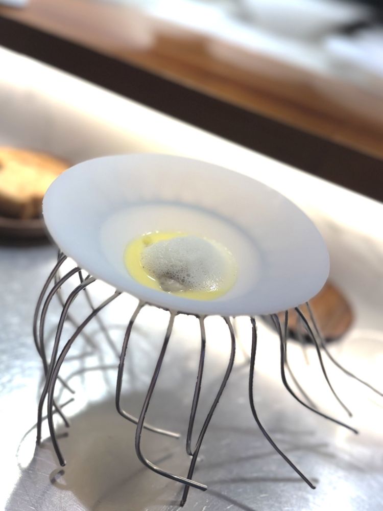 Ostrica al vapore e salsa meunière. Un'ostrica carnosa, generosa nelle dimensioni, viene servita tiepida con una spuma ottenuta dalla stessa e una salsa meunière (mugnaia) a base di burro nocciola, succo di limone e prezzemolo fresco. La temperatura tiepida ne amplifica la consistenza e rende il boccone avvolgente