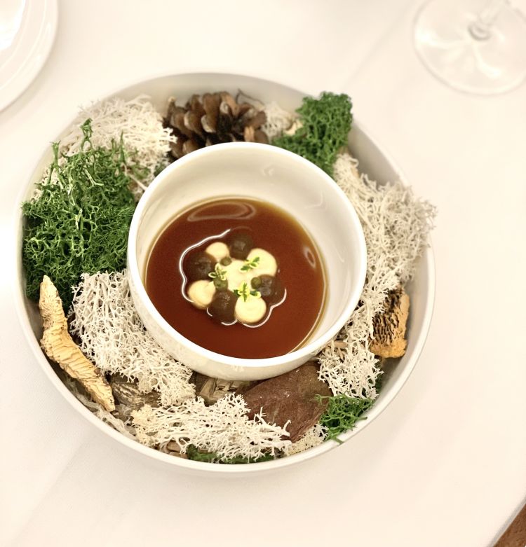 L'inizio è un'immersione diretta nell'habitat caccia - sottobosco, flora e selvaggina insieme. Un brodo di bosco - funghi e, in infusione, maggiorana ed erbe - incontra nel piatto una crema 100% nocciola, un gel di funghi e l'estratto di rosmarino. Accanto, viene servita una cialda con tartare di cervo, foie gras e tarufo. Sebbene parliamo di bosco, la maggiorana avvicina il Mediterraneo; c'è freschezza e un'acidità vicina a quella del pomodoro; la nocciola avvolge, il fungo crea movimento con il suo umami. La carne, fresca, offre la masticazione e lascia spazio a tutta la lunghezza del foie gras, intervallata dal fresco delle erbe aromatiche che tornano
