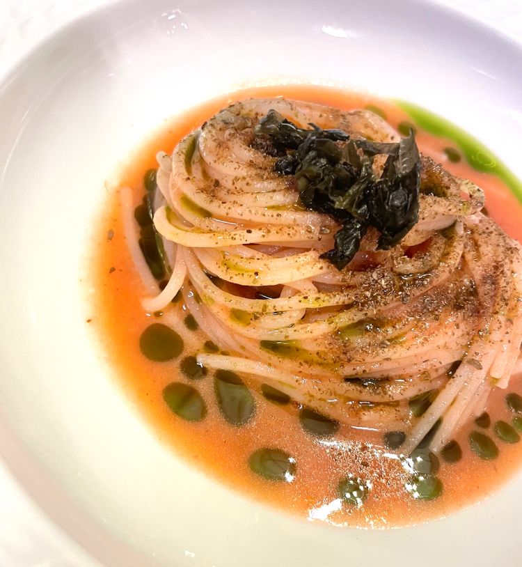 Spaghettino tiepido, fragole, 'nduja, aglio orsino e capperi
Le fragole vengono estratte a caldo e persiste così la loro dolcezza, ma anche un'acidità leggera che a tratti ricorda quella del pomodoro. È l'aglio orsino, sia in olio, sia fermentato, ad apportare un timbro umami, supportato dalla 'nduja - ancora in olio - che avremmo desiderato sentire con più forza. Tutto questo condisce uno spaghettino sottile sottile, quasi impercettibile sul palato; complice la temperatura, il gusto di questo piatto si concentra ulteriormente 
