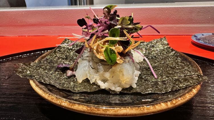 Temaki aoi ebi
Mazzancolla blu Normandia, la sua testa in tempura, yuzu kosho
Su una base di alga nori poggia una mazzancolla blu della Normandia cruda, la sua testa in tempura, germogli di shiso rosso, shiso verde, daikon, sesamo e una salsa yuzu kosho (una salsa piccante con una lunga tradizione in Giappone: si tratta di una pasta cremosa e densa, composta da scorza di yuzu e peperoncino). Il commensale avvolge l’alga nori trattenendo tutti gli ingredienti al suo interno, poi mangia  il temaki con le mani
