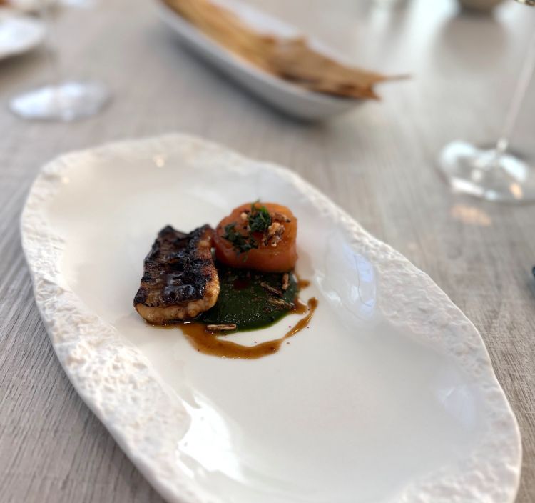 La prima portata &egrave; un'Anguilla con mela, shiso e salsa teriyaki. L&rsquo;anguilla alla brace, laccata con salsa teriyaki, viene proposta con mela caramellata e salsa balsamica allo shiso. La cottura valorizza la componente grassa del pesce, mentre l&rsquo;acidit&agrave; erbacea della salsa e la dolcezza controllata della mela alleggeriscono il boccone, costruendo un insieme ben calibrato. Il piatto si ispirato a un viaggio in Giappone dello chef, che ha voluto portare in tavola i sapori del Sol Levante.&nbsp;In abbinamento un Verdicchio dei Castelli di Jesi Doc Classico Superiore "da Solo" Cantina Terralibera 2023
