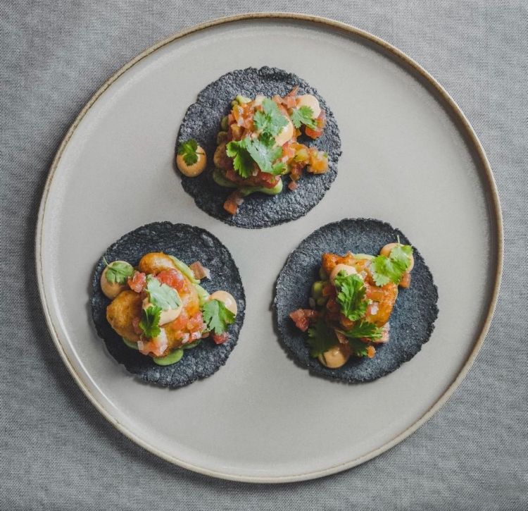 Tacos, purea di avocado, gamberi in tempura, salsa pico de gallo, maionese al chipotle e coriandolo. Un altro dei piatti firma dello chef, i suoi tacos (con tortilla di mais fatta in casa) con gamberi in tempura, purea di avocado, maionese al chipotle (peperoncino messicano affumicato) e coriandolo, e salsa pico de gallo (un classico condimento messicano composto da pomodori, cipolle e peperoncini tritati, ma anche coriandolo, origano, avocado, cumino e limetta). I tacos sono deliziosi con gamberi in tempura croccanti che si sposano molto bene con la dolcezza del guacamole e la piccantezza della maionese. Un piatto che vale il viaggio. Chapeau! Con il vino rimaniamo sempre in Alto Adige con l’azienda Hofstätter, ma questa volta proviamo il loro Pinot Grigio 2024.