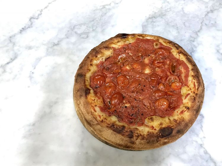 La "pizza del giorno dopo" di Franco Pepe, impasto doppio in teglia condito semplicemente con pomodoro, cipolla, aromi