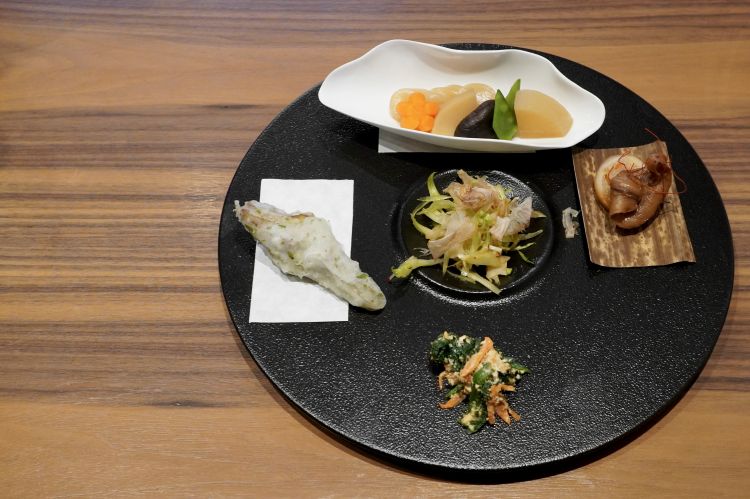 Appetizer: dal basso in senso orario basso, Tofu con spinaci, carote e salsa goma ai semi di sesamo; Tempura di carciofo con pastella alla alga nori; Konnyaku (amido di patata) con carota, germoglio di bambù, shiitake, taccole e daikon stufato; Ikameshi (ossia calamaro ripieno stufato e marinato in salsa di soia). Al centro, Insalata di puntarelle, radici di loto e katsuobushi