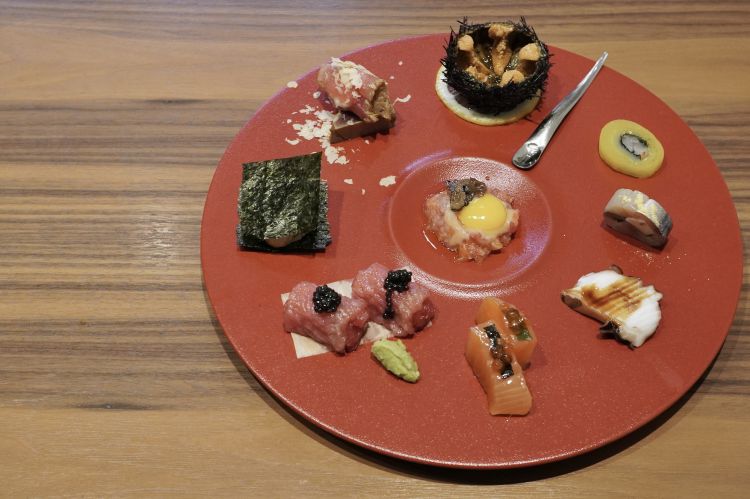 Dal basso a sinistra, in senso antiorario: Ventresca di tonno con caviale; Bocconcini di salmone (marinati tre giorni nel miso) con uova di salmone in soia e yuzu; Polpo bollito con aceto balsamico; Sgombro marinato sotto sale e in aceto di riso con igname cinese, shiso, alga nori, gari (lo zenzero giapponese) e polvere di yuzu; Takuan (daikon marinato) con calamaro crudo, nori e amaebi (gamberi dolci); Riccio di mare giapponese al naturale; Zuke maguro (filetto di tonno marinato) con scaglie di noce e gorgonzola; Millefoglie di capasanta scottata, nori e lardo al tartufo bianco. Al centro, Tartare di tonno, salmone e ricciola con salsa yuzumiso, tuorlo di uova di quaglia e tartufo nero
