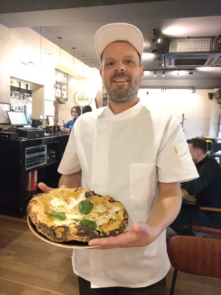 Il pizzaiolo Goran Misevski mi porta orgoglioso la pizza da me scelta: Ciao, amore con datterini gialli, fiordilatte, provola affumicata, olio extravergine, origano, 4 tipi di pepe e basilico