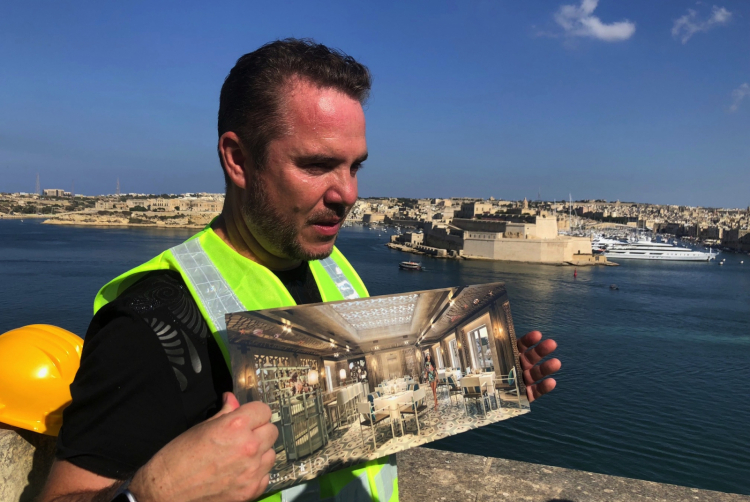 Patron Mark Weingard with renderings of the project, still a building site. Behind him, Fort Saint Angelo 
