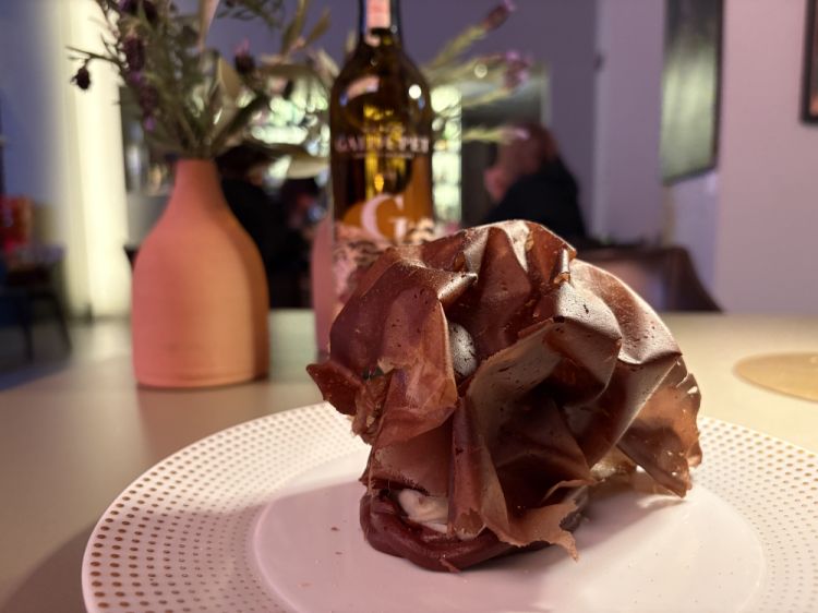 Fondente - Cioccolato, bergamotto e rafano
«Quando affondi il cucchiaio in questo dolce, si trova una parte croccante. Si chiama carta cacao in termini tecnici: vengono stese una ad una e poi messe nel forno a caldo, creando poi la forma che si vede nel piatto: è un lavoro che brucia un po' le mani, se ne fanno due alla volta, è tosto insomma. Però ha questa leggerezza che ci piace molto. Sotto invece c'è una parte molto più avvolgente, una ganache. Il bergamotto, che adesso sta per andare fuori stagione, ci piace usarlo tanto. E poi il rafano, perché ci piaceva mettere un elemento che è normalmente legato ai bolliti, alla cucina salata, in un dolce. Col cioccolato secondo noi convive molto bene»