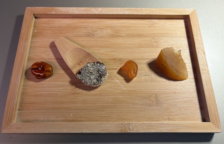 Saluto dalla cucina
«Partendo da sinistra troviamo il cupuaçu, che è un seme amazzonico, l'unico ingrediente che abbiamo in cucina che arriva da così lontano. Perché insieme ad altri ristoratori abbiamo deciso di aiutare la comunità che coltiva il cupuaçu a non sparire, e a non far sparire neanche il seme, perché siamo in pochissimi ad utilizzarlo, non ha tanto mercato in Europa. Quindi chi coltiva questo frutto sta togliendo le piante per dar spazio ad allevamenti o avocado. Questa comunità ci ha chiesto di aiutarli, abbiamo scoperto questo seme e l'abbiamo caramellato per lasciarlo vedere in modo tale che fosse vitreo, quasi come fosse un gioiello. Poi abbiamo un mou al ginepro con sopra del lievito e per finire gli agrumi canditi che abbiamo fatto a febbraio: bergamotto e kumquat»