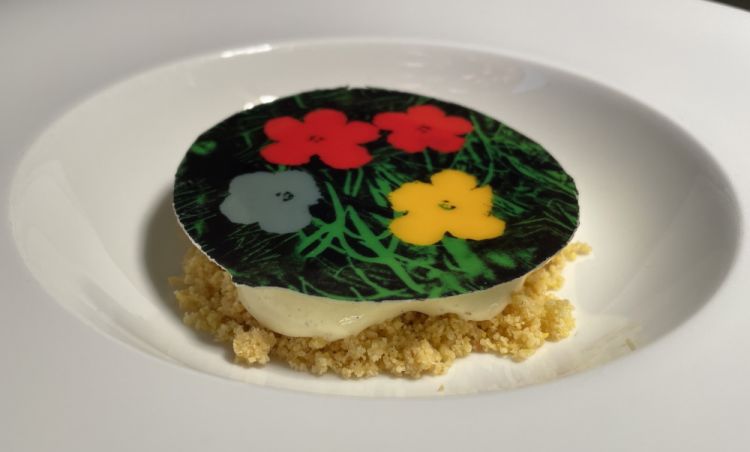 Pop flowers: gallette, vermut e fiori
«Il dessert è ispirato al lavoro di Andy Warhol, e alla sua opera Flowers. L'abbiamo poi legato alla cultura pop, rappresentata dalla pizza di gallette: quindi un biscotto inzuppato nel vermut, con crema pasticciera. Abbiamo fatto una spuma creata con biscotti, gallette, imbevute nel vermut, con una base di crema inglese con un'infusione delle erbe che si usano per il vermut, quindi sambuco e camomilla. Poi c'è un terzo richiamo, collegato all'arancia e all'orange blossom, i fiori di arancia: questo perché durante il proibizionismo in America si usava diluire il vermut con il succo di arancia, per sfuggire ai controlli. Quindi in questa ricetta i fiori hanno tre diverse dimensioni: la citazione di Warhol, l'infuso e l'orange blossom»
