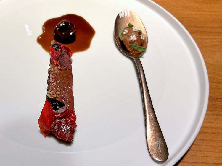 Anatra laccata, umeboshi: petto d’anatra laccato con il suo jus, ciliegia fresca, salsa bigarade (brodo ridotto di anatra, caramello sfumato con birra di ciliegie e agrumi), cous cous fritto, fiori di peonie, sul cucchiaino fegatini di anatra con umeboshi, infine brodo di anatra con fave al vapore e cosce d’anatra caramellate sfilacciate
