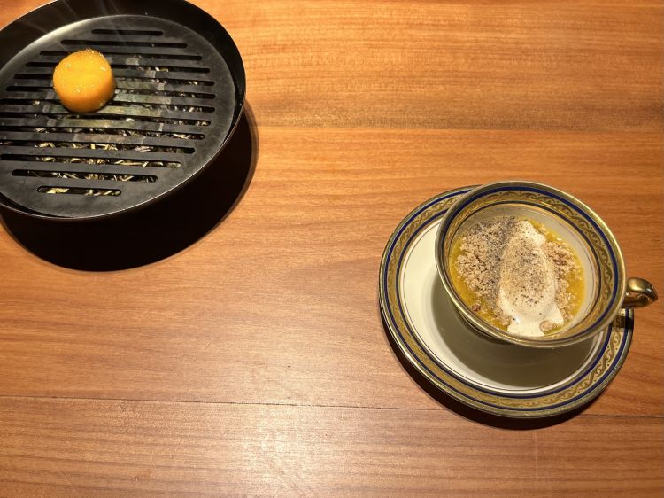 Mango: sulla griglia è cotto confit e affumicato col fieno; nella tazza una zuppa acida con mango e lemongrass, acqua di ananas cotta in osmosi con cime di coriandolo, gelato alla vaniglia, pepe affumicato e crumble di grano saraceno
