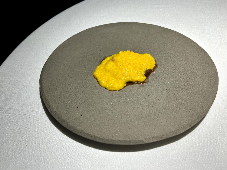 Risone, sgombro, uvetta, zafferano, tra la pasta con le sarde e il riso alla milanese. Il risone viene mantecato con zafferano e burro affumicato allo sgombro, alla base un carpaccio di sgombro affumicato che viene laccato con una riduzione di uvetta, infine midollo di vitello